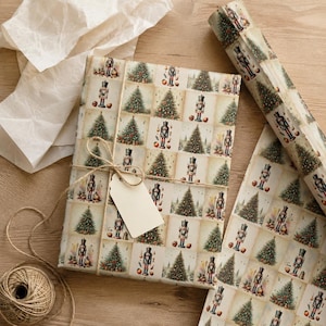 Pode incluir: Um presente retangular embrulhado em papel creme com um padr&atilde;o de grade repetitivo de quebra-nozes ilustrados e &aacute;rvores de Natal decoradas. O pacote est&aacute; amarrado com um cord&atilde;o castanho fino e inclui uma etiqueta de papel retangular em branco.