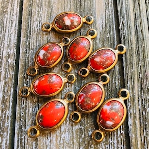 Puede incluir: Ocho abalorios conectores ovalados de piedra roja y blanca con detalles metálicos dorados. Los abalorios tienen dos lazos a cada lado para sujetar a las joyas.