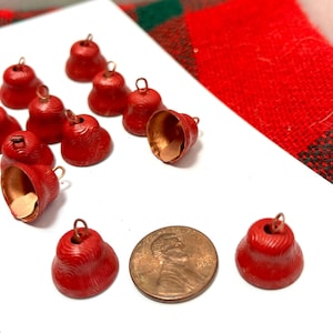 Peut inclure: Une collection de 11 petites cloches en métal rouge avec un intérieur en cuivre. Les cloches ont une surface texturée et sont enfilées sur un fil fin.