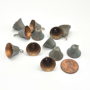 Puede incluir: Un conjunto de diez pequeños dijes en forma de campana con una pátina azul verdosa desgastada en el exterior y un interior texturizado de color cobre. Cada campana tiene un pequeño lazo de metal en la parte superior. Se incluye una moneda de cobre.
