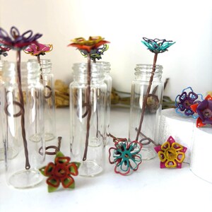 Puede incluir: Botellas de vidrio transparente con flores de alambre de colores y tallos marrones. Las flores son de varios colores, incluyendo rojo, amarillo, rosa y turquesa. Algunas flores est&aacute;n dentro de las botellas.