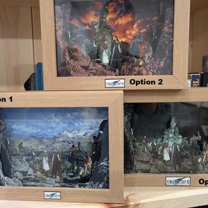 May include: Three framed shadow box art pieces depicting scenes from Final Fantasy VII. Each piece contains a detailed diorama with miniature figures set against a backdrop. The frames are light-coloured wood, and each has a Final Fantasy VII logo.