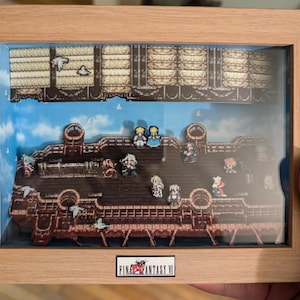 May include: A framed 3D pixel art piece depicting a scene from Final Fantasy VI. The scene features a ship with characters standing on the deck. The frame is made of wood and has a glass front.