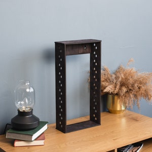 Pode incluir: Uma estante de madeira preta com uma moldura retangular e uma série de furos igualmente espaçados. A estante está sobre uma mesa de madeira.