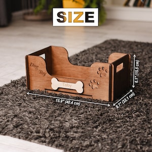 May include: A wooden dog bed with the words "Dog Toy" and "Toby" engraved on it. The bed measures 15.9 inches by 8.7 inches by 6.1 inches.