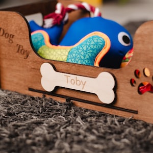 May include: A wooden dog toy box with a bone-shaped name tag that says "Toby". The box is filled with a blue and green dog toy.