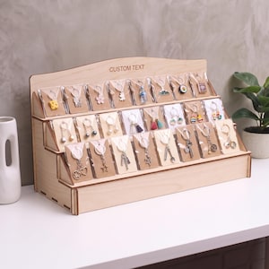 May include: A tiered wooden display stand with the text CUSTOM TEXT printed on the top edge. The stand features multiple rows of individual keychains, each packaged in a clear plastic sleeve on a rectangular cardboard backing card.
