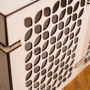 May include: A wooden box with a geometric pattern cut out of the front. The pattern is made up of small, oval shapes that are arranged in a repeating pattern.