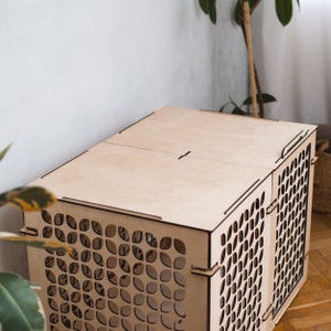 May include: A wooden cat carrier with a geometric pattern. The carrier has a hinged top and is made of light wood.
