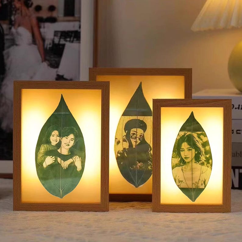 May include: Three wooden picture frames with a light brown finish. Each frame features a leaf design with a photo inside. The photos are of people smiling. The frames are illuminated from behind.