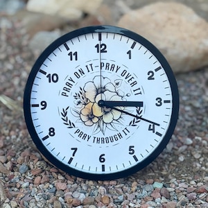 May include: A black and white clock with floral accents and the text "Pray on it - Pray over it - Pray through it".