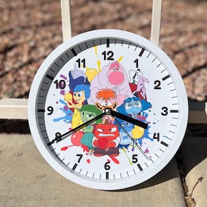 May include: White round clock with a colorful design featuring characters from the movie Inside Out. The clock face has black numbers and hands. The characters include Joy, Sadness, Anger, Fear, and Disgust.