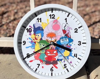 May include: White round clock with a colorful design featuring characters from the movie Inside Out. The clock face has black numbers and hands. The characters include Joy, Sadness, Anger, Fear, and Disgust.