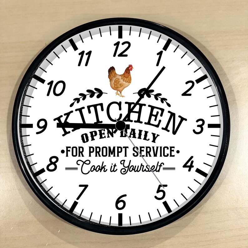 May include: A black and white kitchen clock with a white background and black numbers. The clock has a black border and a black hand. The clock face says "Kitchen Open Daily - For Prompt Service - Cook it Yourself" with a picture of a chicken.