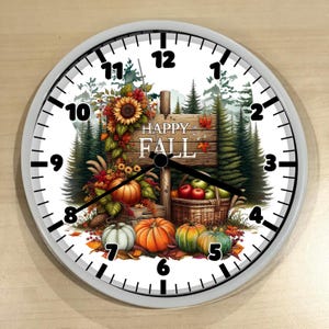 May include: A round wall clock with a white face and a gray frame. The clock face features a fall-themed design with pumpkins, a sunflower, and the words "HAPPY FALL". The clock hands point to approximately 3:50.