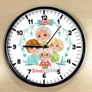 May include: A round wall clock with a black frame. The clock face features an illustration of four women with the text "THANKS FRIENDS" and "FOR BEING MY". The clock hands are black and red.