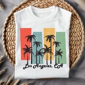 May include: White t-shirt with a vintage-style graphic of palm trees and the text "Los Angeles, CA".