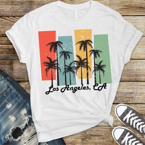 May include: White t-shirt with a vintage-style graphic of palm trees and the text "Los Angeles, CA".
