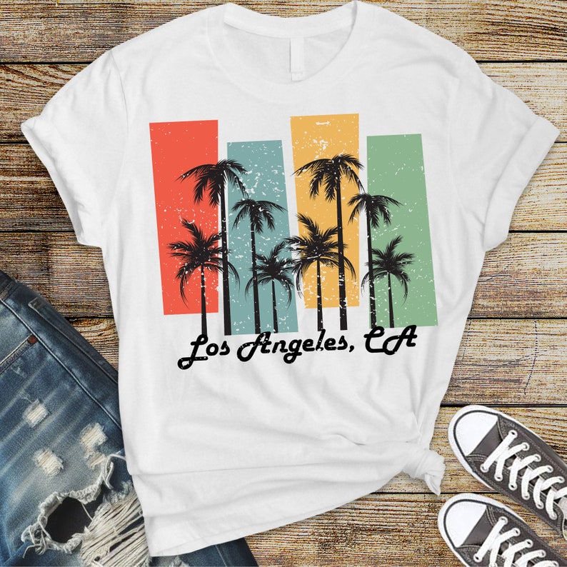 May include: White t-shirt with a vintage-style graphic of palm trees and the text "Los Angeles, CA".
