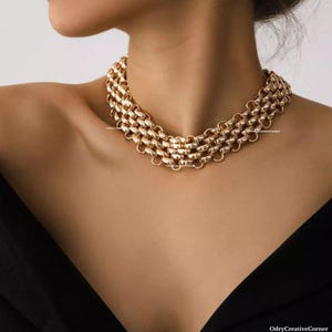 May include: A gold chain necklace with a layered, chunky design. The necklace is made of multiple rows of linked circles.