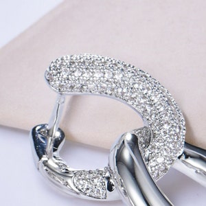 May include: Silver hoop earrings with a linked design, featuring a pave setting of clear cubic zirconia stones.
