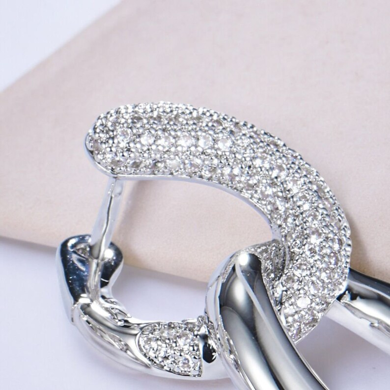 May include: Silver hoop earrings with a linked design, featuring a pave setting of clear cubic zirconia stones.