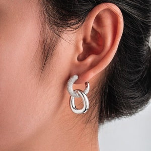 May include: Silver hoop earrings with a double chain design. The earrings are encrusted with small, clear stones.