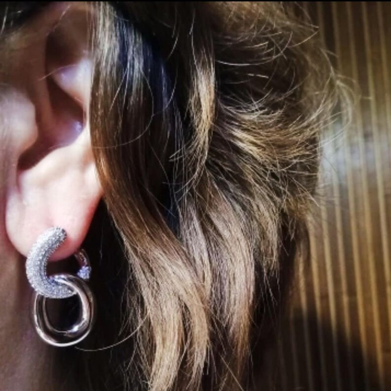 May include: Silver hoop earrings with a small, sparkly design. The earrings are made of two hoops, one larger than the other, that are connected together.