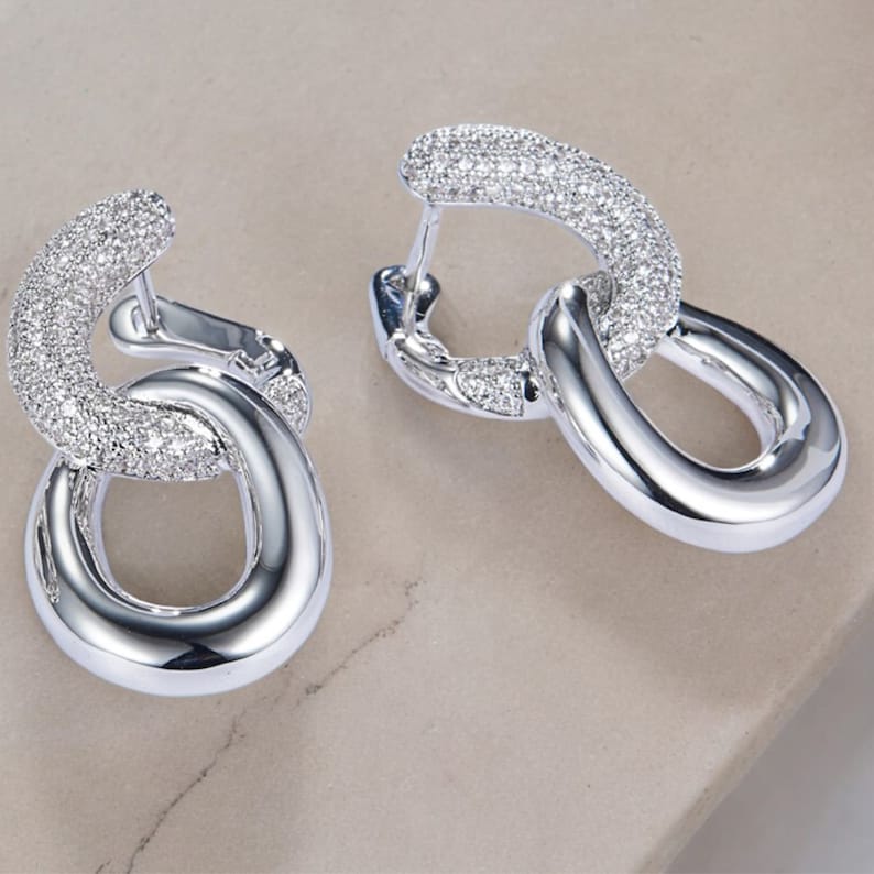 May include: A pair of silver hoop earrings with a linked design. The hoops are encrusted with small, clear stones.