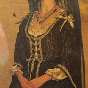 May include: A woman wearing a black and gold brocade dress with a lace-up bodice and a long black veil. She is wearing a gold necklace and earrings.