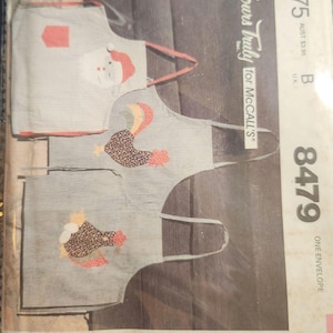 May include: A vintage McCall's pattern envelope featuring three apron designs. One apron has a Santa Claus applique, and the other two feature rooster appliques. The envelope has the text "Yours Truly for McCall's" and the number "8479".