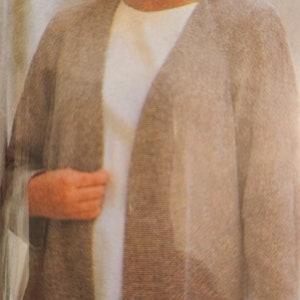 May include: A woman wearing a light brown cardigan over a white shirt. The cardigan has a long, open front and a relaxed fit.