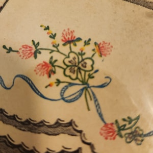 May include: A vintage floral design with a blue ribbon bow. The design features red, green, and yellow flowers with a four-leaf clover in the center.