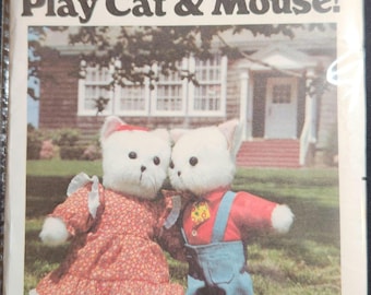 Puede incluir: Un patrón de costura Butterick vintage titulado "Play Cat & Mouse!" con dos muñecos de gato de peluche. Uno lleva un vestido floral rojo, el otro una camisa roja y un peto azul. El número de patrón es 5666.