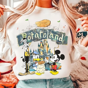 May include: White sweatshirt with a cartoon illustration of Mickey Mouse, Goofy, and Donald Duck. The illustration features a castle and the text "Potatoland".