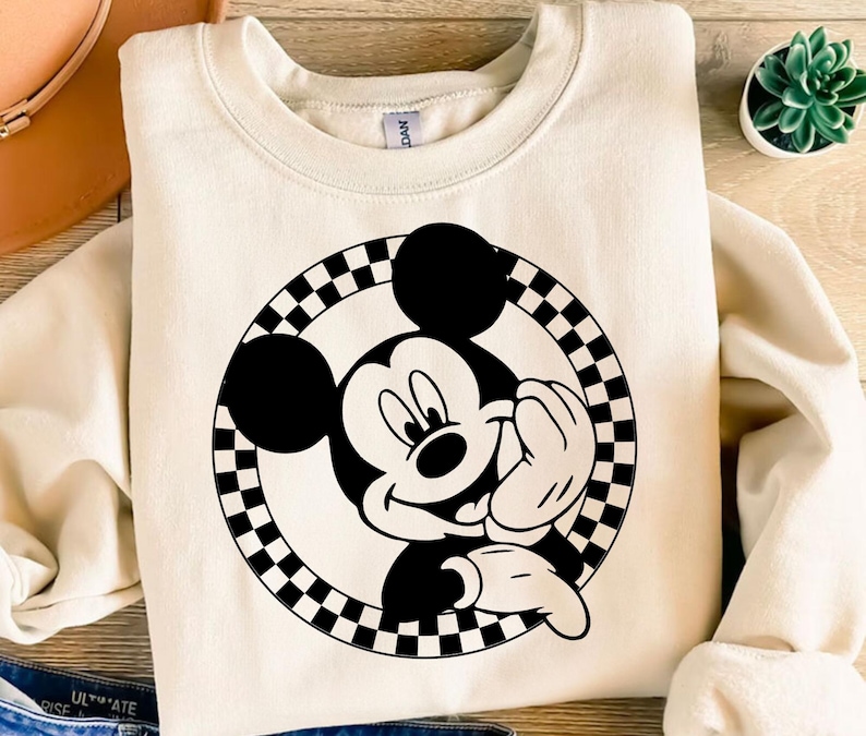 K&ouml;nnte beinhalten: Cremefarbenes Sweatshirt mit einem schwarz-wei&szlig;en Mickey Mouse-Motiv. Die Grafik zeigt Mickey Mouse, die in einem karierten Kreis l&auml;chelt. Das Sweatshirt hat einen Rundhalsausschnitt und lange &Auml;rmel.