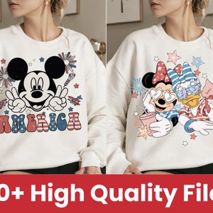 May include: Two white sweatshirts with a patriotic theme. One features Mickey Mouse with the word "America" in red, white, and blue. The other features Minnie Mouse and Daisy Duck wearing red, white, and blue outfits.