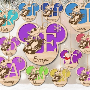 May include: Twelve wooden ornaments shaped like Mickey Mouse ears with a cutout of the character Jack Skellington from the movie The Nightmare Before Christmas. Each ornament has a different letter of the alphabet and a name, such as Kylie, Isaac, Evelyn, and Chloe.