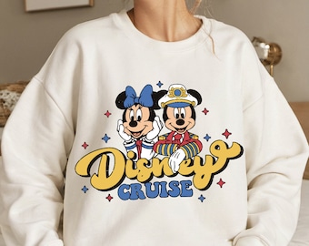 May include: White sweatshirt with a graphic of Mickey Mouse and Minnie Mouse dressed as a captain and a sailor. The text "Disney Cruise" is printed in yellow on the sweatshirt.