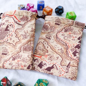 May include: Two brown fabric dice bags with a map design. The bags have red stitching and a drawstring closure. The bags are surrounded by colorful dice.