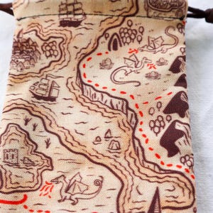 May include: A beige fabric dice bag with a brown drawstring closure. The bag features a printed design of a map with ships, dragons, and a red dotted line.