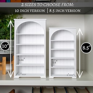 以下が含まれることがあります： アーチ型のトップと複数の棚を備えた2つの白い木製本棚。 大きな本棚は高さ25.4cm、小さな本棚は高さ21.6cmです。 画像にはテキストが含まれています: "2つのサイズからお選びいただけます: 10インチバージョン | 8.5インチバージョン."