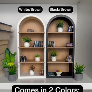 May include: Two arched shelves, one white and one black, with brown shelves and a corkboard back. Each shelf is decorated with potted plants and books. The text "White/Brown" and "Black/Brown" is above each shelf. The text "Comes in 2 Colors" is below the shelves.
