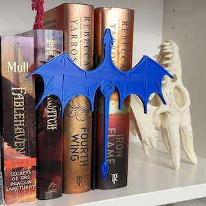 May include: A blue dragon bookend with wings spread wide, holding up four books with titles including "Iron Flame", "Fourth Wing", "Watch", and "Fablehaven".