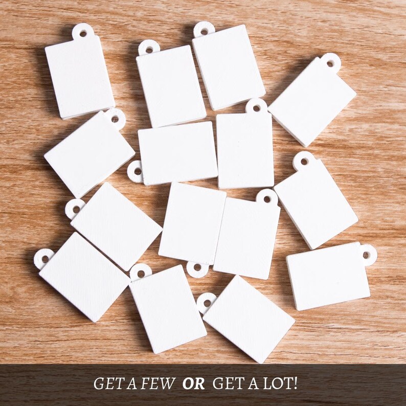 May include: A selection of small, white rectangular tags with a circular hole at the top, arranged on a wooden surface. The tags are plain, possibly for personalisation or labelling. The text at the bottom reads "GET A FEW OR GET A LOT!"