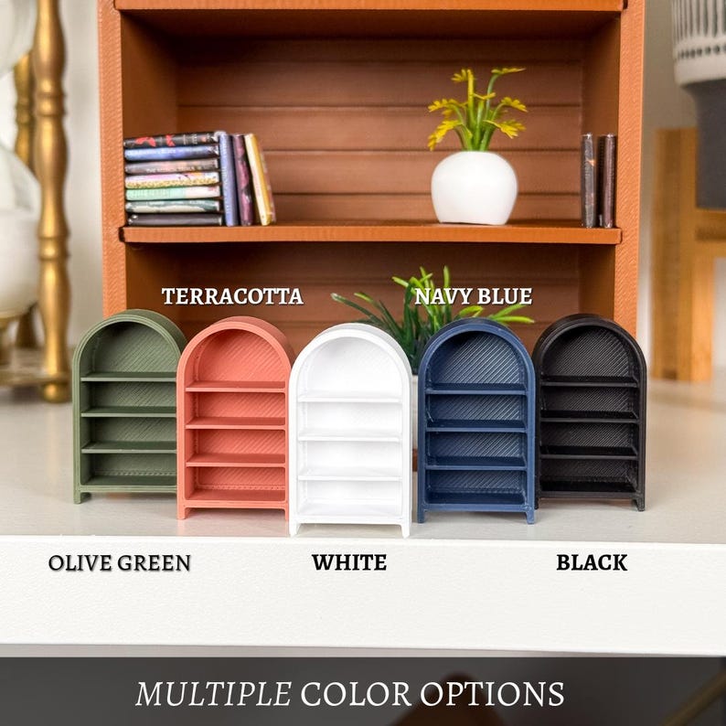 May include: Miniature arched bookshelves in olive green, terracotta, white, navy blue, and black. The shelves have three tiers and are labeled with their respective colors. The text "MULTIPLE COLOR OPTIONS" is at the bottom.