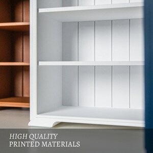 以下が含まれることがあります： 2 つの棚と背面に垂直パネルを備えた白い木製キャビネット。背景には茶色の木製キャビネットが見えます。下部のテキストは「HIGH QUALITY PRINTED MATERIALS」と書かれています。収納に最適です。