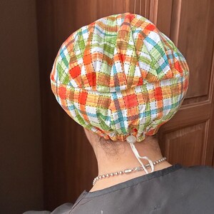 May include: A plaid fabric scrub hat with a white drawstring. The hat is tied at the back of the neck.