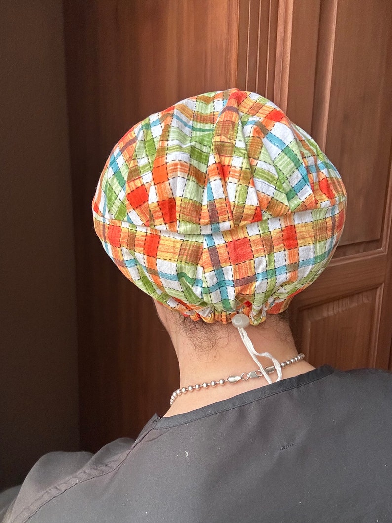 May include: A plaid fabric scrub hat with a white drawstring. The hat is tied at the back of the neck.