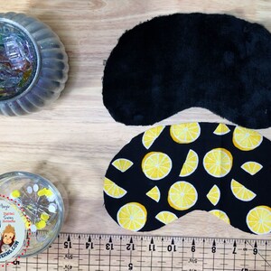 May include: Two pieces of fabric for a sleep mask. One piece is black velvet and the other is black with a yellow lemon print. A ruler is in the bottom of the image.